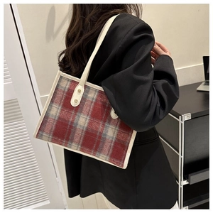 Detail view of red tartan tote bag with cream leather trim and metal rivets