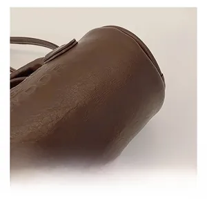 Detail view of brown textured leather bag showing precise stitching and embossed logo