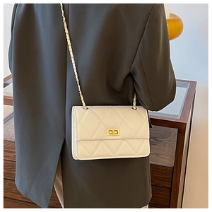 Vue détaillée du sac matelassé blanc avec chaîne dorée sur un blazer gris chic