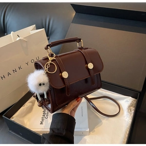 Detail of dark brown retro handbag with gold hardware and plush charm in a gift box