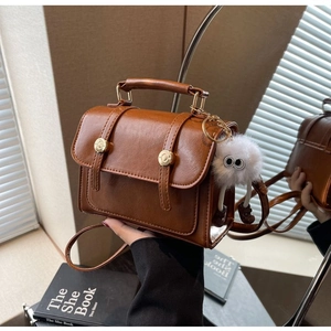 Detail of vintage brown leather handbag with metal buckle and plush ball charm accessory