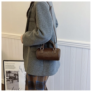 Detail of dark brown vintage cylinder bag with embossed logo and adjustable shoulder strap