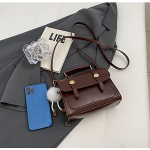 Close-up of retro brown faux leather messenger bag with gold buckles and plush charm