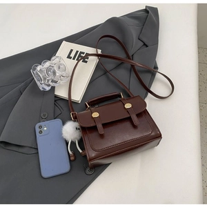 Detail view of a retro dark brown crossbody bag with gold hardware and plush charm