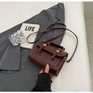 Detail of vintage brown crossbody bag with gold hardware on a grey blazer backdrop