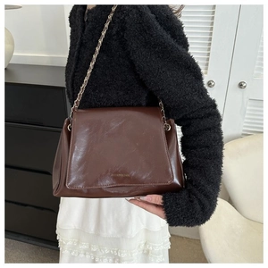 Detail of dark brown glossy leather tote bag with elegant gold metal chain strap