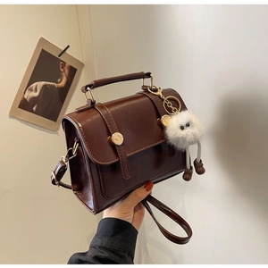 Detail of dark brown vintage mini bag with gold buckle and white plush charm accessory