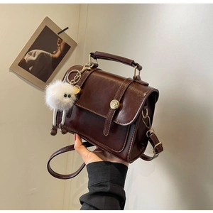Detail of dark brown glossy retro handbag with fluffy white charm and thin strap