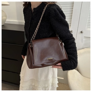 Detailed close-up of dark brown glossy leather shoulder bag with gold chain strap