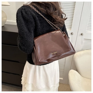 Detail of dark brown glossy leather tote bag with gold chain strap and embossed text