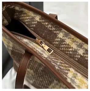 Detail eines goldenen Reißverschlusses an einer braunen Tweed-Tasche mit Webstruktur