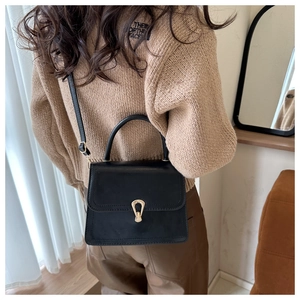 Detailed view of black square bag with gold shield lock worn by a model in casual style