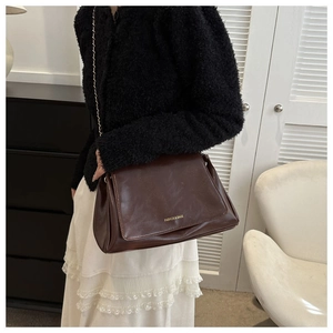 Macro shot of dark brown glossy leather shoulder bag with golden chain strap