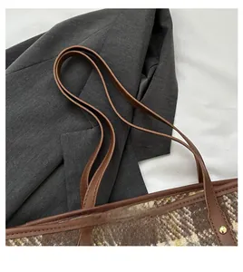 Detail der karierten Tweed-Tasche mit braunem Ledergriff und goldenen Nietendetails