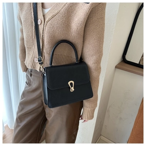 Detail of a black leather handbag with a gold horseshoe buckle shown on a model