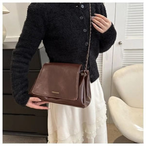 Detail of dark brown faux leather crossbody bag with gold chain strap on model