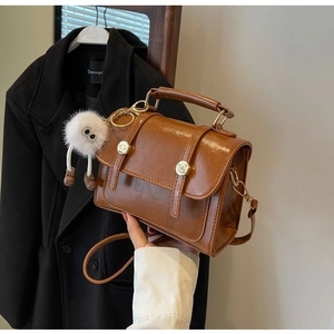 Close-up of brown retro leather handbag with plush charm and gold metallic buckles