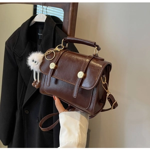 Detail view of dark brown glossy leather handbag with gold rivets and cute white charm