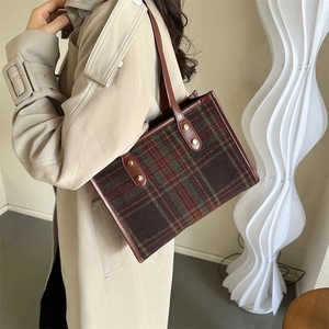 Plaid wool tote bag with brown leather handles and gold studs worn by a model