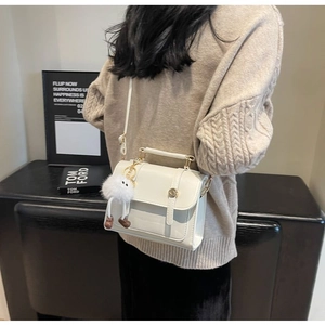 Chic off-white mini crossbody bag with plush charm shown worn by a model in a cozy setting