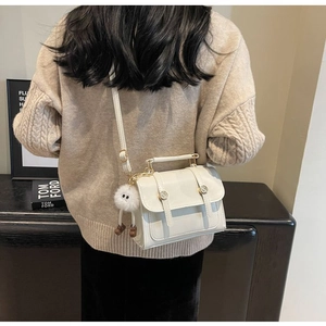 Detail of cream small square crossbody bag with metal buckles and plush charm on a model
