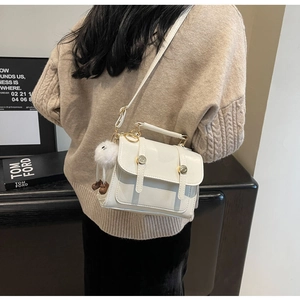 Close-up of a cream white leather square handbag featuring golden buckles and a fur ball
