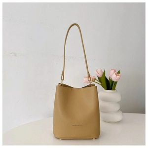 Detail of khaki bucket bag with textured leather and gold strap hardware on white table
