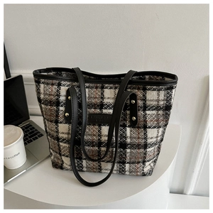 Detail der karierten Tweed-Tasche mit Ledergriffen und Goldnieten auf weißem Tisch