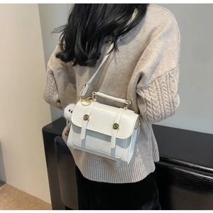 Detail of white crossbody bag with gold hardware and plush pompom charm on a model
