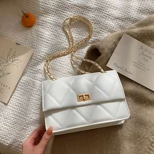 Sac à bandoulière matelassé blanc avec chaîne dorée et fermoir rotatif sur fond texturé
