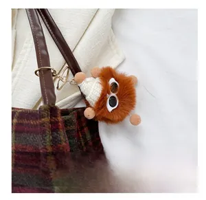 Detailed view of a brown plush monster bag charm with a gold clasp on a checkered tote