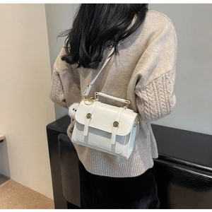 White minimalist leather crossbody bag with gold buckles and plush pompom charm detail