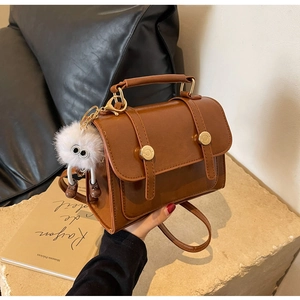 Detail of vintage caramel square bag with plush monster charm and shiny PU leather finish