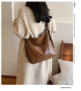 Brown leather tote bag worn by a model in a beige coat showing side pocket detail