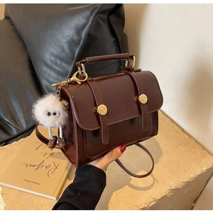 Detail of vintage brown crossbody bag with gold hardware and white plush charm accessory