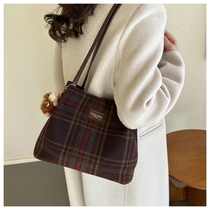 Detail of vintage plaid woolen tote bag with leather strap and plush charm on white coat
