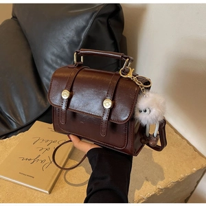 Detail of dark brown vintage crossbody bag with glossy finish and plush pendant
