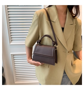 Détail d'un sac à main en cuir mat marron foncé avec une poignée nouée au design unique
