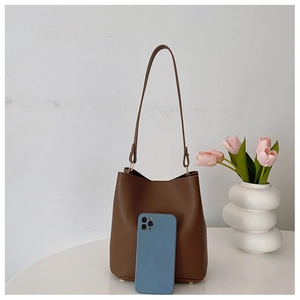 Macro detail of dark brown litchi grain leather bucket bag with phone for scale