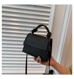 Détail d'un sac à main en cuir noir mat avec poignée nouée et rabat minimaliste