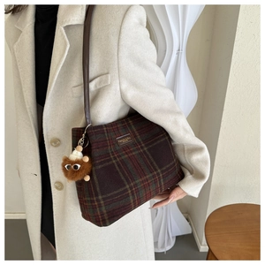 Detailed close-up of wool plaid tote bag featuring a leather tag and plush monster charm