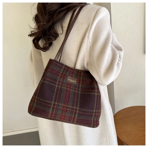Detail of wool plaid tote bag featuring red and green checks with a leather label