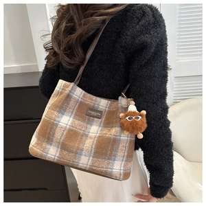 Detail of wool plaid tote bag featuring a plush monster charm and leather brand tag