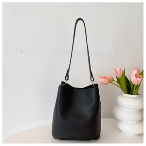 Detail of black lychee grain leather bucket bag with slim strap on white podium