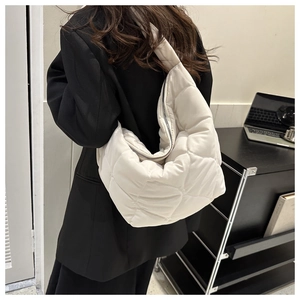 Detail of white quilted puffer shoulder bag in glossy nylon fabric worn by model