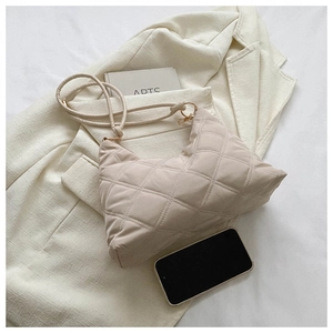 Detail of beige quilted shoulder bag with diamond stitching on a modern blazer background
