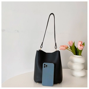 Detail view of large black lychee leather bucket bag with phone for scale reference