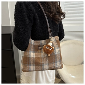 Detail of plaid wool tote bag featuring a leather logo tag and brown plush doll charm