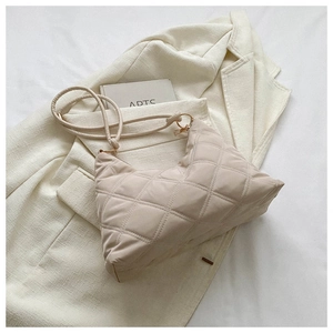 Detail view of quilted beige shoulder bag with diamond stitching and gold hardware
