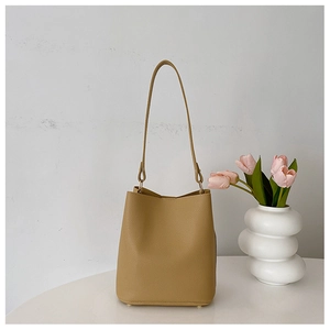Detail of khaki lychee grain bucket bag featuring a long shoulder strap and metal feet